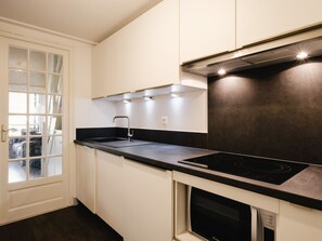 A modern kitchen with white cabinets, a black countertop, a stainless steel range hood, and a built-in oven. - Charming studio near slopes, pets allowed (La Clusaz)