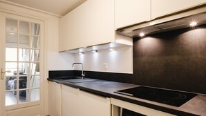A modern kitchen with white cabinets, a black countertop, a stainless steel range hood, and a built-in oven. - Charming studio near slopes, pets allowed (La Clusaz)