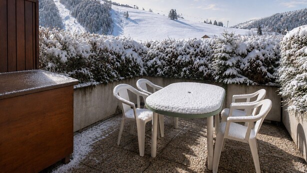 A patio with a table and chairs, overlooking a snowy landscape with trees and a distant hill. - Cozy studio for 4, near slopes and shops, pets welcome, parking included (La Clusaz)
