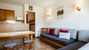 A compact living space with a kitchenette, a sofa with patterned cushions, a dining table with stools, and a small TV. - Cozy studio for 4, near slopes and shops, pets welcome, parking included (La Clusaz)