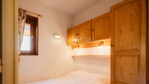 A small, single-bed room with wooden cabinets and a window with floral curtains. - Cozy studio for 4, near slopes and shops, pets welcome, parking included (La Clusaz)
