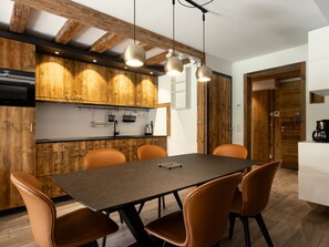 A modern kitchen with wooden cabinets, a dining table with chairs, and pendant lighting.