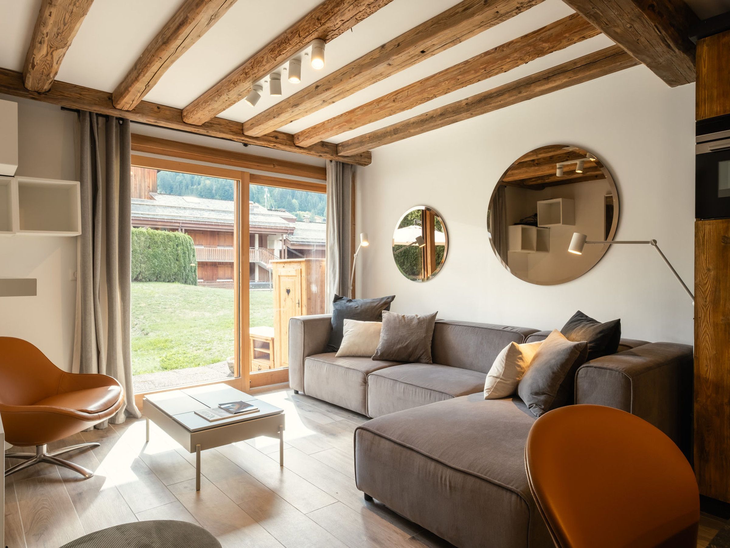 A modern living room with a sofa, chairs, a coffee table, wooden beams, and large windows.