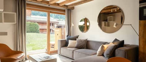 A modern living room with a sofa, chairs, a coffee table, wooden beams, and large windows.