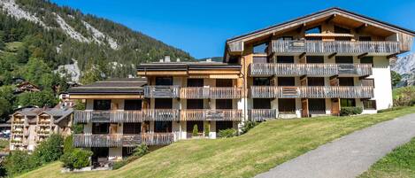 Un hôtel à plusieurs étages doté de balcons en bois, d’un chemin pavé et surplombant un paysage montagneux.