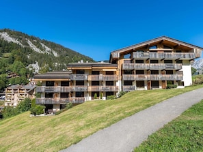 A multi-story hotel with wooden balconies, a paved pathway, and a mountainous backdrop.