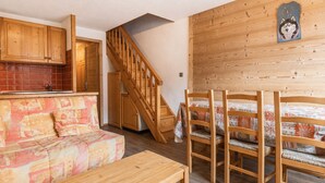 A cozy room with a wooden staircase, a sofa, a dining table, and a bed with patterned bedding. - Perfect ski location, 6 guests, pets, garage, WIFI (La Clusaz)