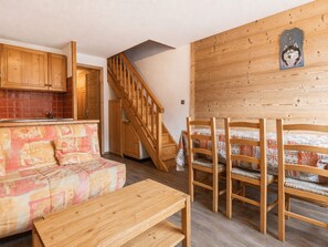 A cozy room with a wooden staircase, a sofa, a dining table, and a bed with patterned bedding. - Perfect ski location, 6 guests, pets, garage, WIFI (La Clusaz)