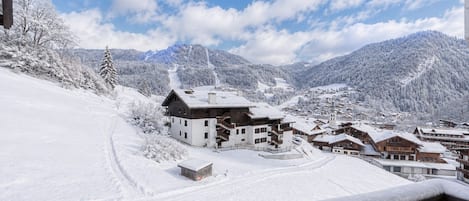 A snow-covered village with wooden buildings, a ski slope, and mountains in the background.