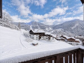 A snow-covered village with wooden buildings, a ski slope, and mountains in the background.