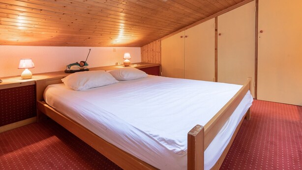 A bedroom with a wooden ceiling, a skylight, a bed with white bedding, two bedside tables with lamps, and a wardrobe. - Perfect ski location, 6 guests, pets, garage, WIFI (La Clusaz)