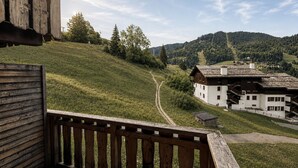 A wooden deck with a view of a white building and a path leading to a mountain. - Perfect ski location, 6 guests, pets, garage, WIFI (La Clusaz)