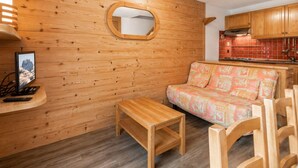 A wooden interior with a sofa, a small table, a TV, and a kitchen area. - Perfect ski location, 6 guests, pets, garage, WIFI (La Clusaz)