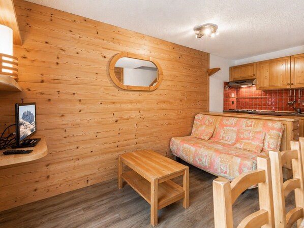 A wooden interior with a sofa, a small table, a TV, and a kitchen area.