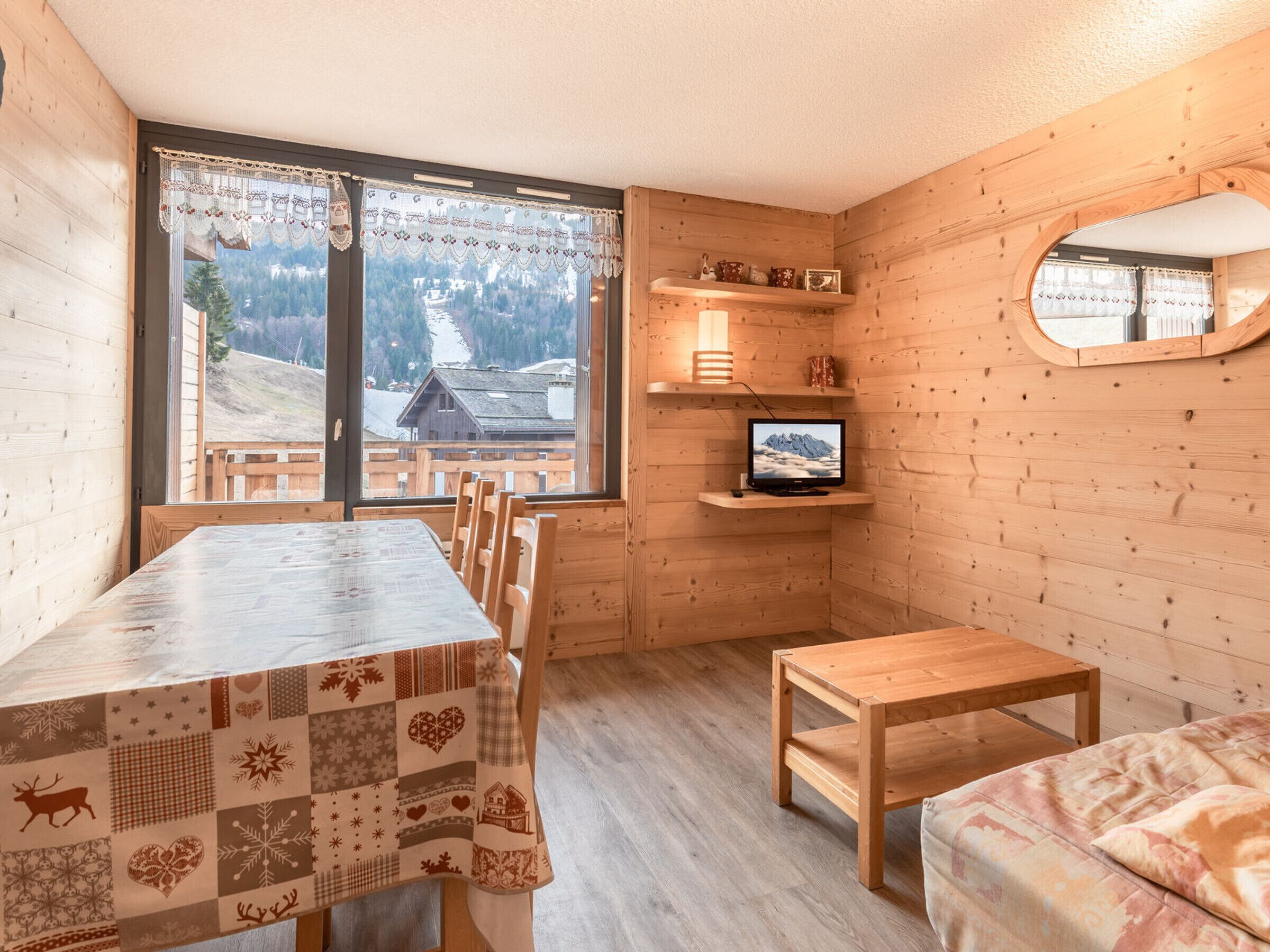 Un chalet confortable avec un intérieur en bois, une table à manger, un téléviseur et une vue sur une montagne enneigée.