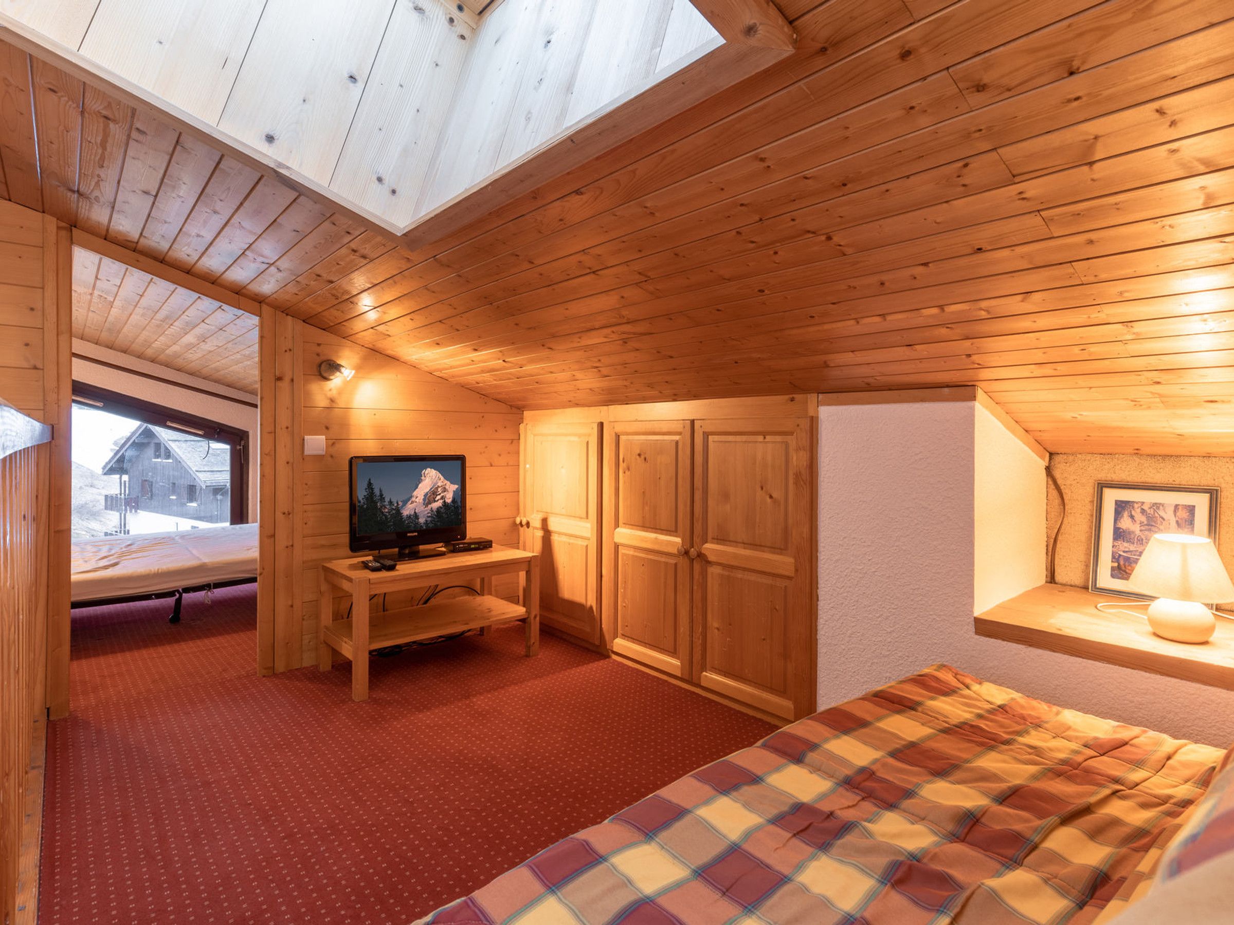 Habitación de cabaña de madera con una cama, un televisor, un escritorio y ventana con vistas a un paisaje nevado.