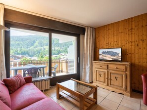 Habitación con sofá, mesa de centro de vidrio, mueble de madera y televisor que muestra una vista de la montaña.