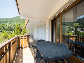Ein Balkon mit Tisch und Stühlen, Blick auf eine bewaldete Landschaft und ein Gebäude mit Holzgeländer.