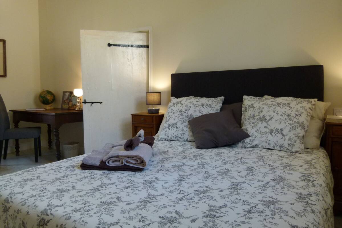 Ein ordentlich bezogenes Bett mit Blumenmuster, eine Nachttischlampe und ein dunkles Kopfteil.