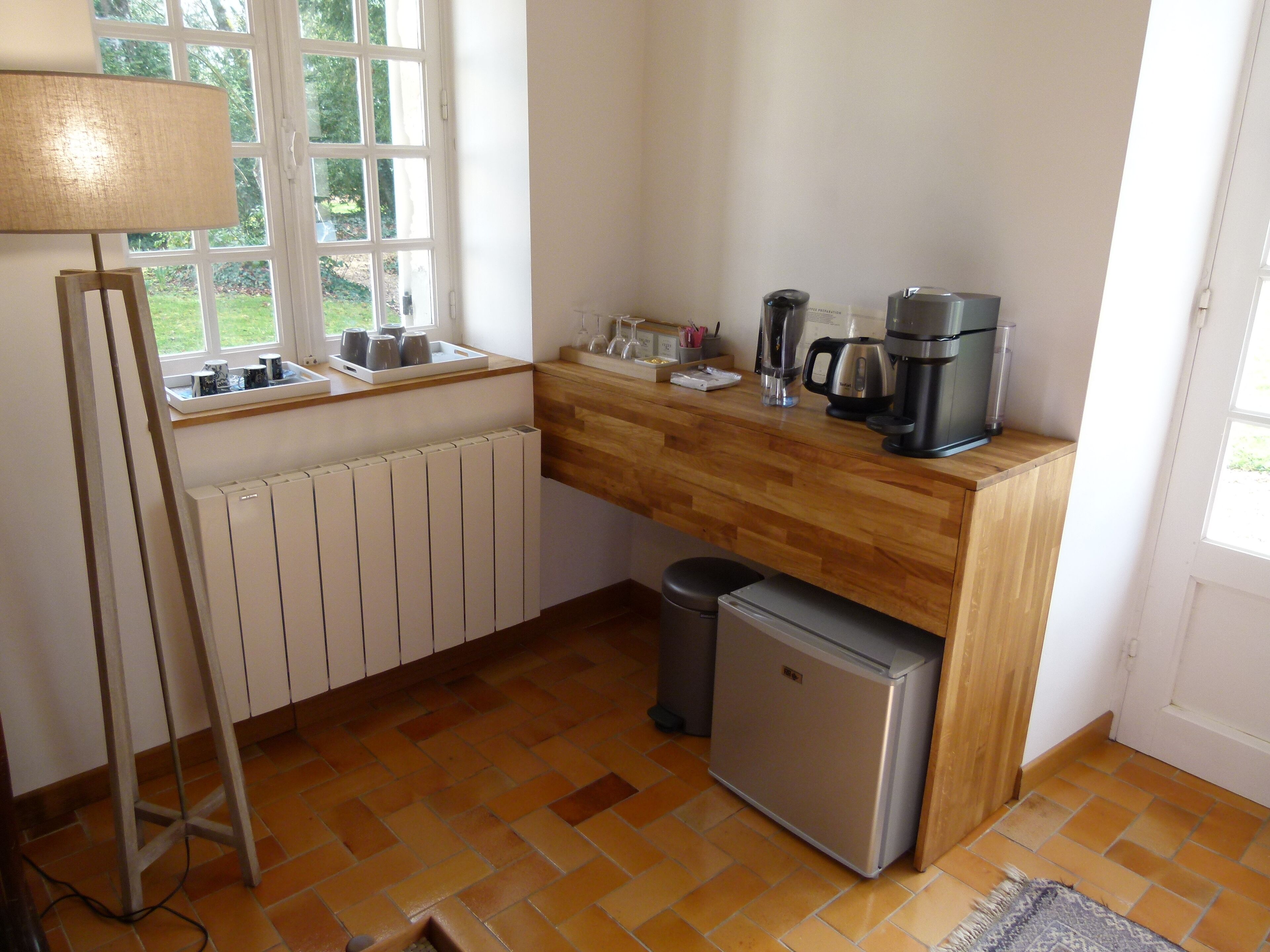 A compact kitchen with a wooden countertop, a small refrigerator, a coffee maker, and a window with a view of greenery.