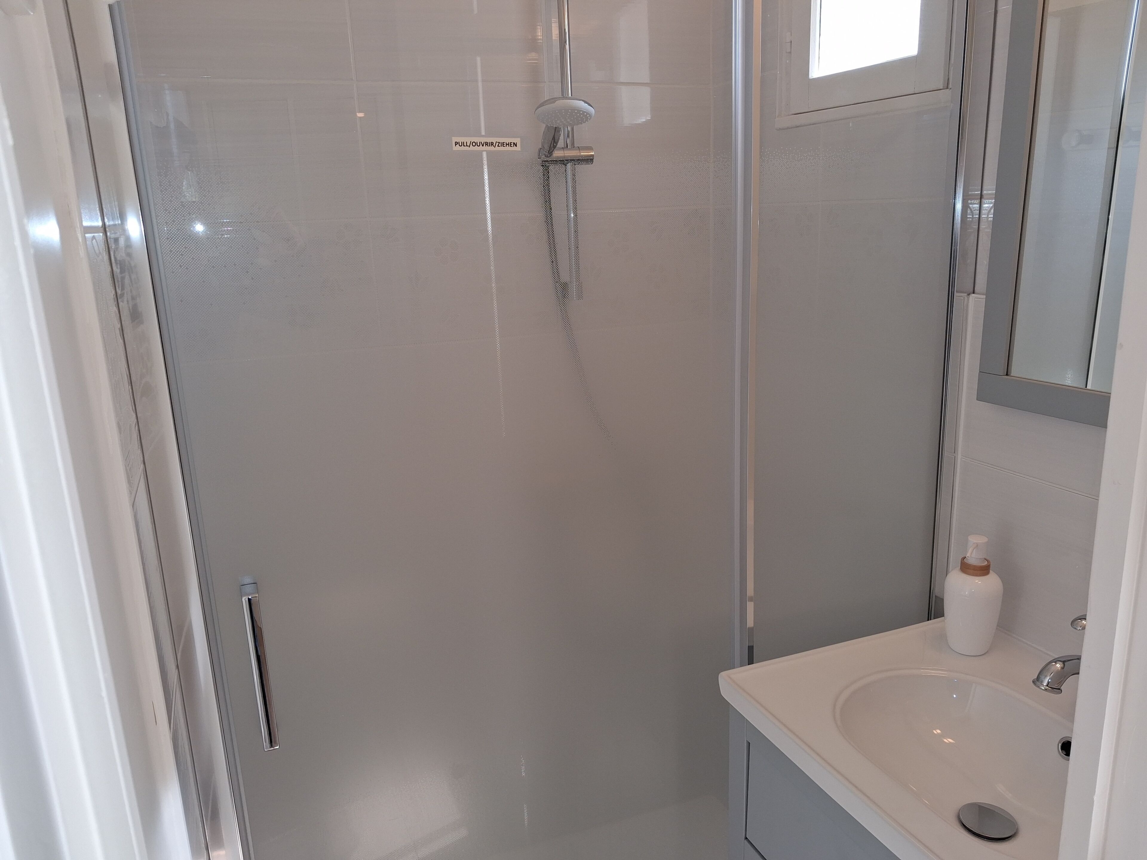 A modern bathroom with a glass-enclosed shower, a white sink, and a mirror above the sink.