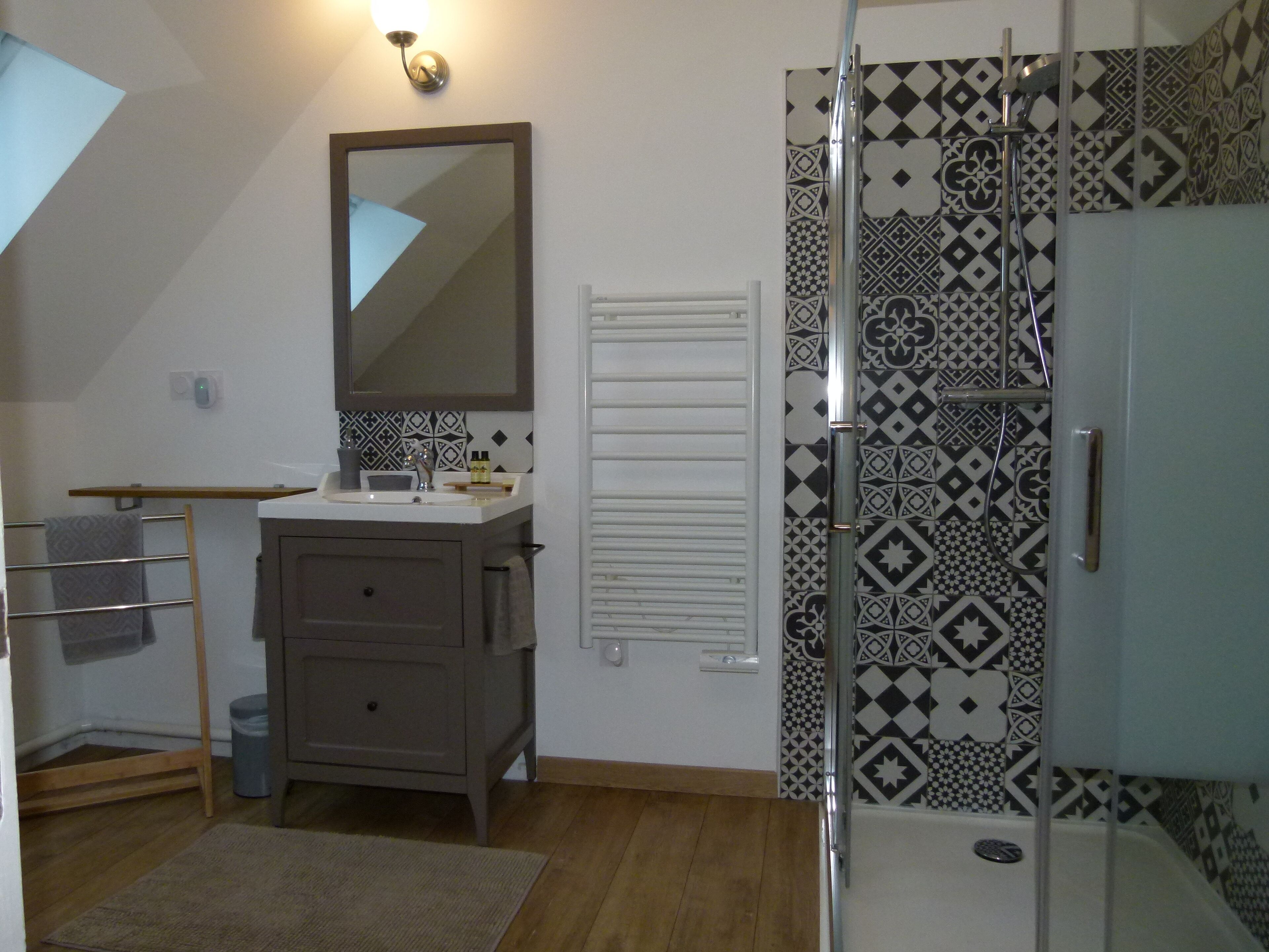 A bathroom with a shower, a sink with a mirror, a towel rack, and patterned tiles.