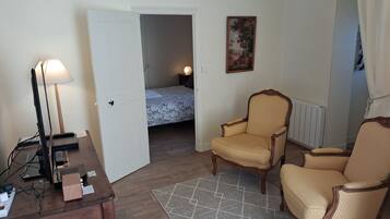 Een kamer met een bureau, twee fauteuils, een bed, een schilderij en een radiator.
