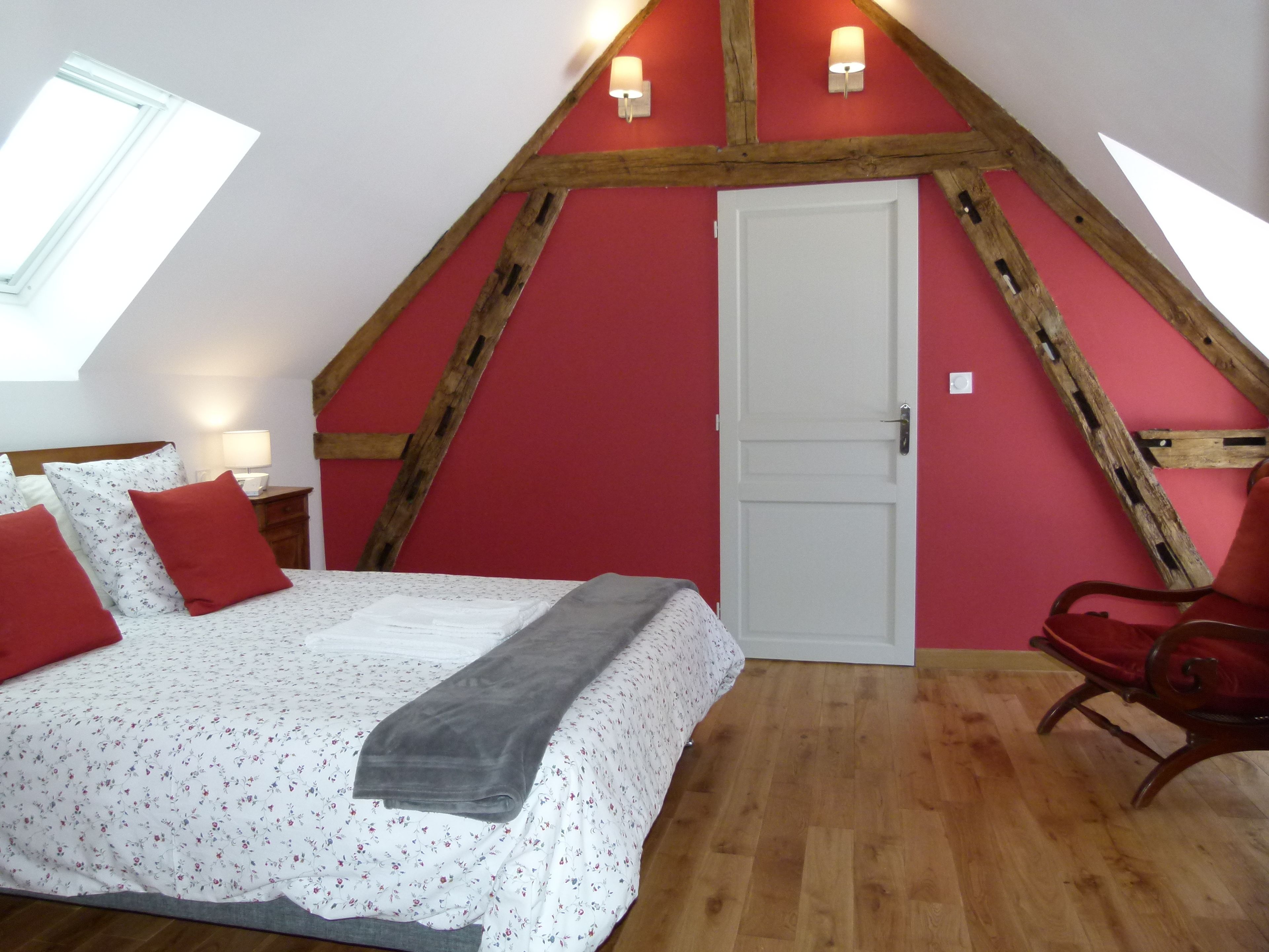A bedroom with a sloped ceiling, a bed with floral bedding, red pillows, a wooden chair, and a white door.