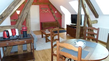 Une pièce mansardée chaleureuse, avec une table en bois, des chaises, un téléviseur et un mur rouge.