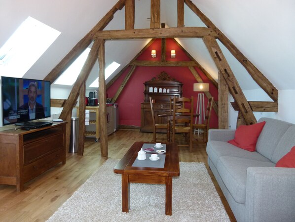 Habitación estilo loft con techo de madera, televisor, mesa de comedor y sofá.