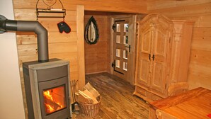 A cozy room with a wood-burning stove, a wooden cabinet, and a table. - Haus Anni im Paradies (Kiefersfelden)