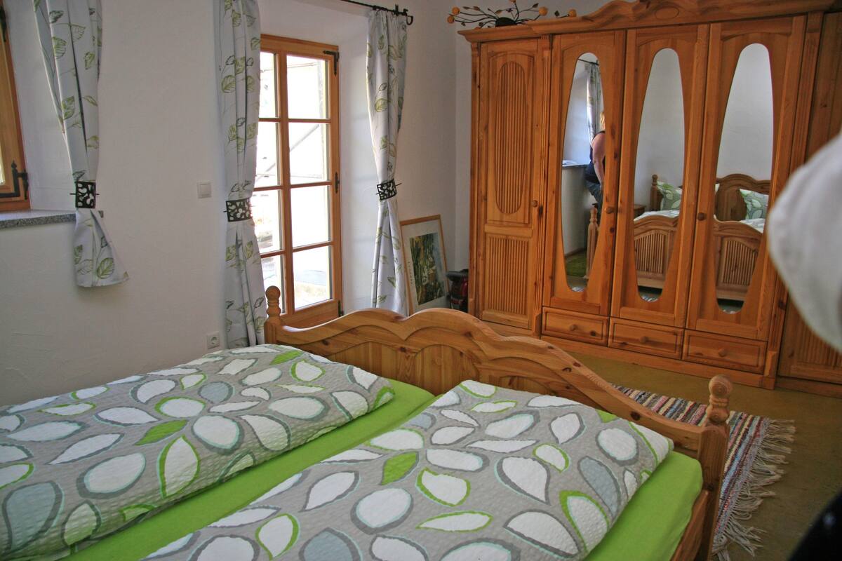 A bedroom with two single beds, a wooden wardrobe, and a window with curtains.