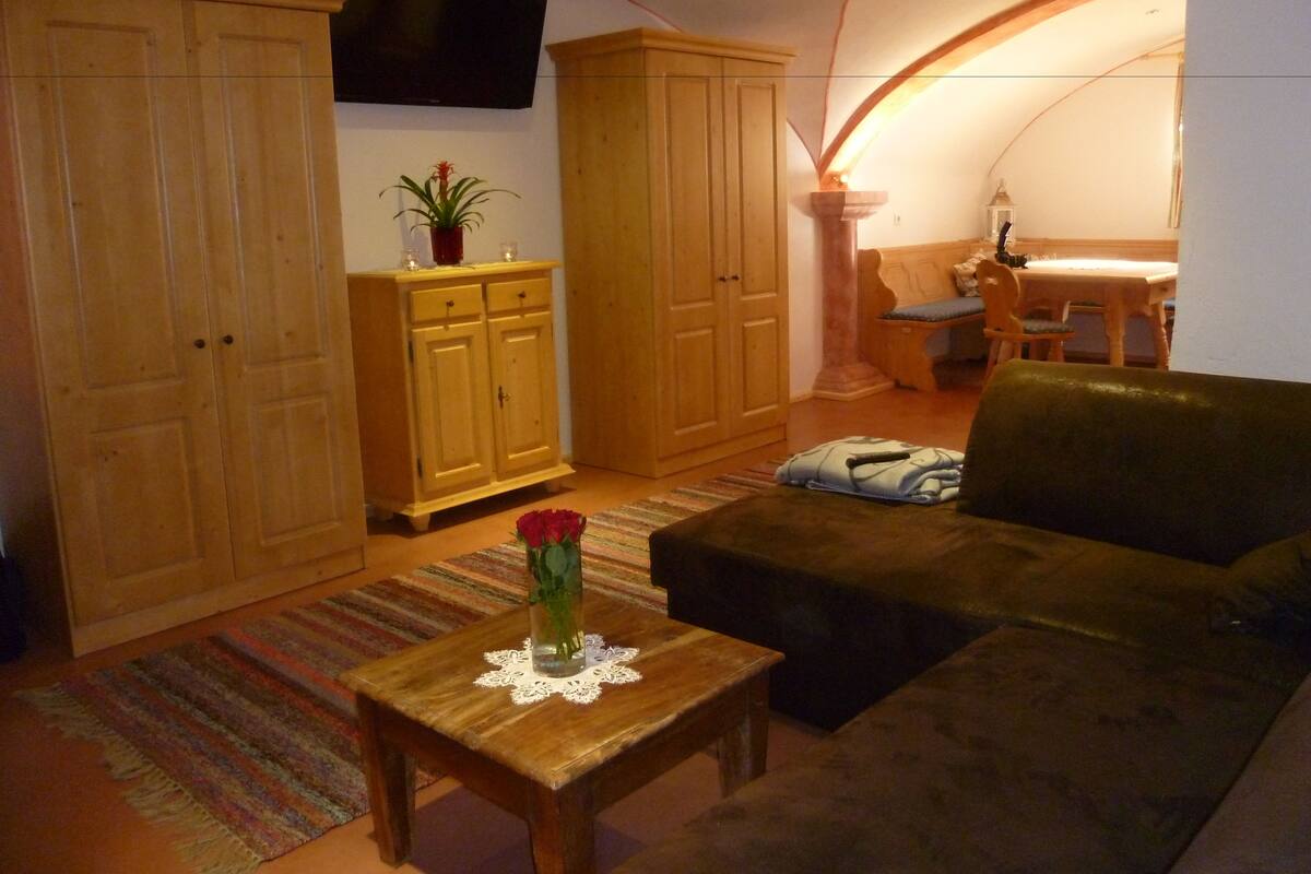 A cozy living room with a sofa, a wooden table with a vase, and a television mounted on the wall.