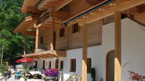A wooden building with a sloped roof, multiple windows, and a red umbrella. - Haus Anni im Paradies (Kiefersfelden)