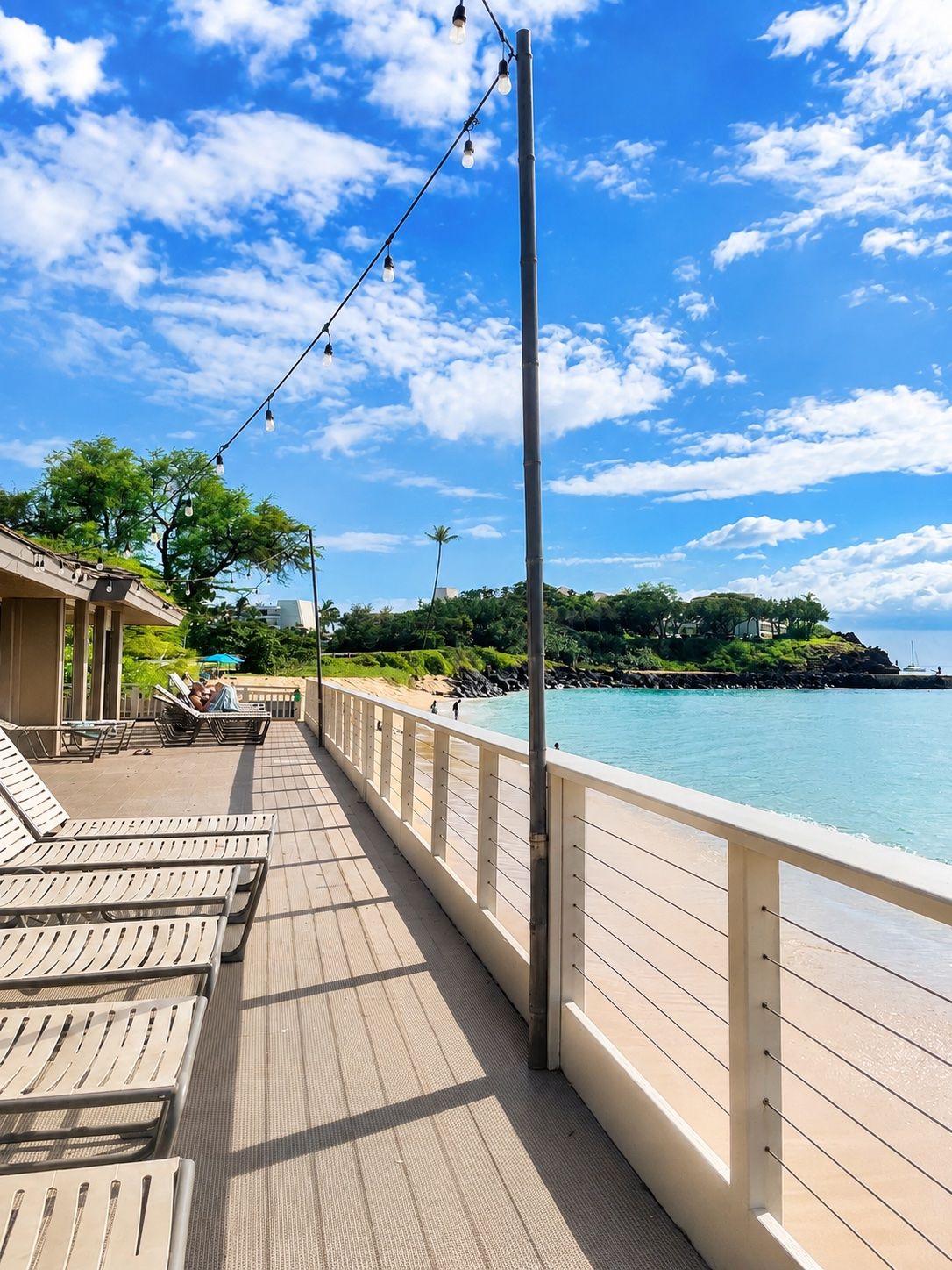 Eine Holzterrasse mit Liegestühlen, einem Geländer und Blick aufs Meer.