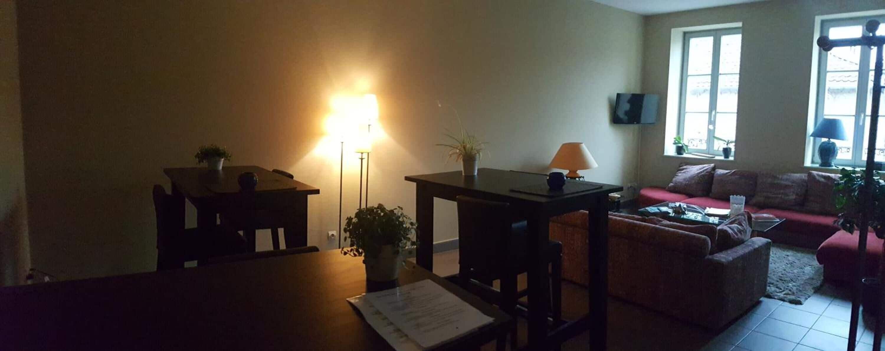 A living room with a dining table, a sofa, and a TV mounted on the wall.