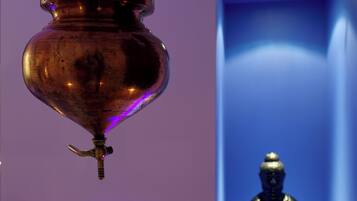 A hanging copper vessel with a spout, a statue of a seated figure, and a blue-lit corridor.