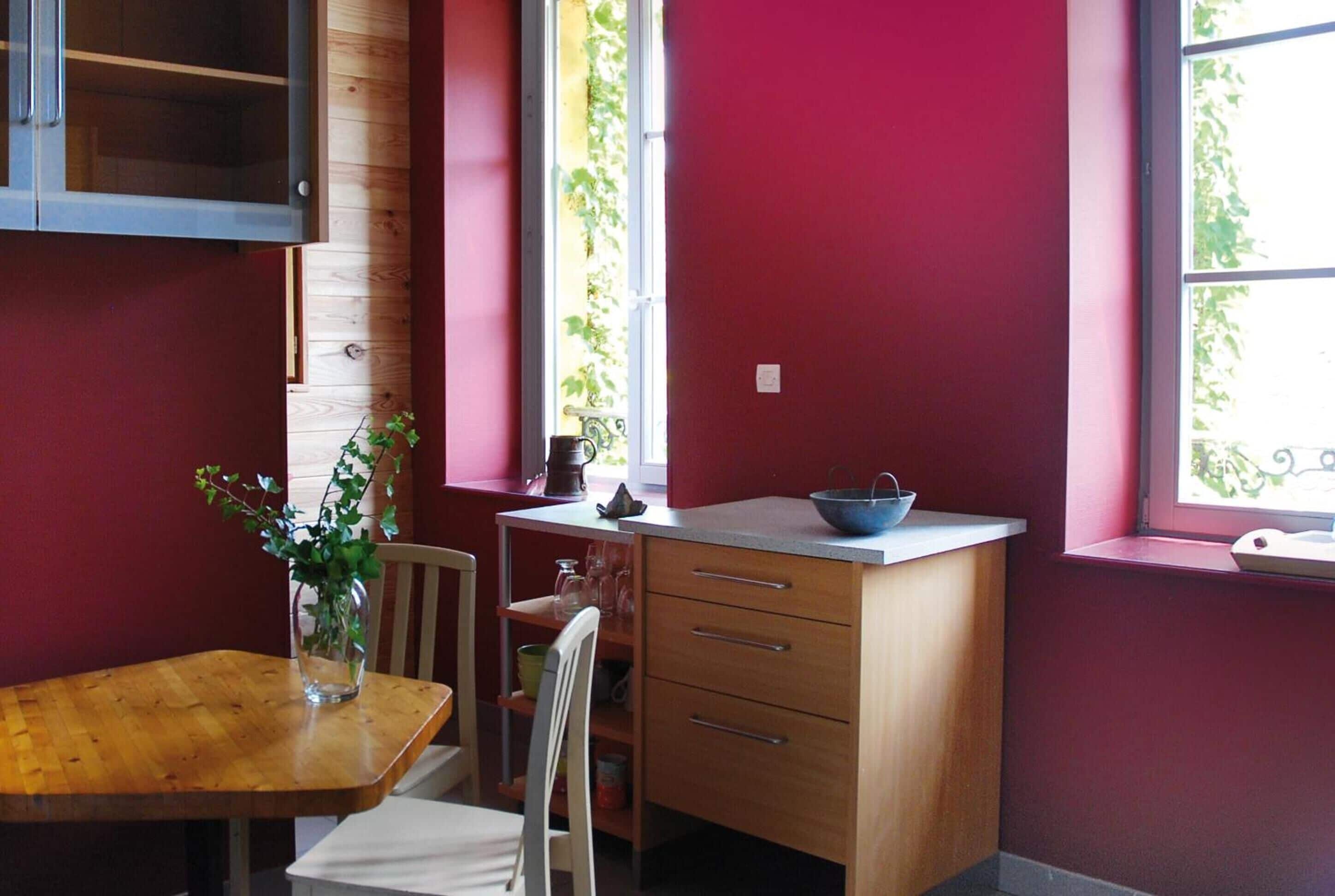 A compact kitchen with a wooden table, a white chair, a small cabinet, and a window with a view of greenery.