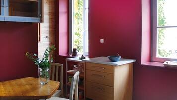 A compact kitchen with a wooden table, a white chair, a small cabinet, and a window with a view of greenery.