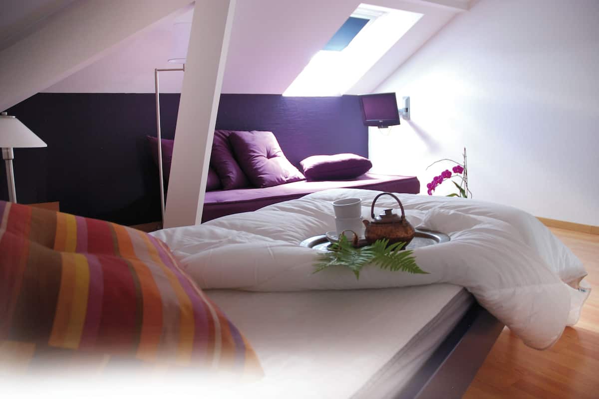 A bedroom with a bed, a bedside table, a lamp, a window, and a view of the outside.