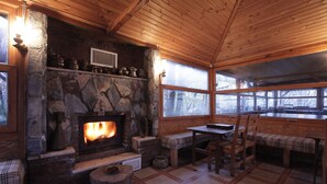 A cozy cabin interior with a stone fireplace, wooden furniture, and large windows. - Karaca Dag Evleri (Basiskele)