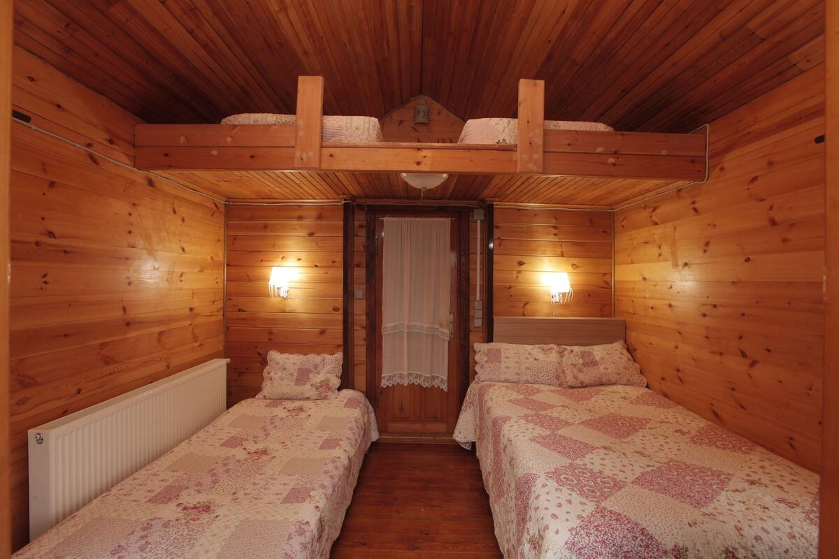 A wooden cabin room with two beds, a ceiling fan, and a door with a curtain.