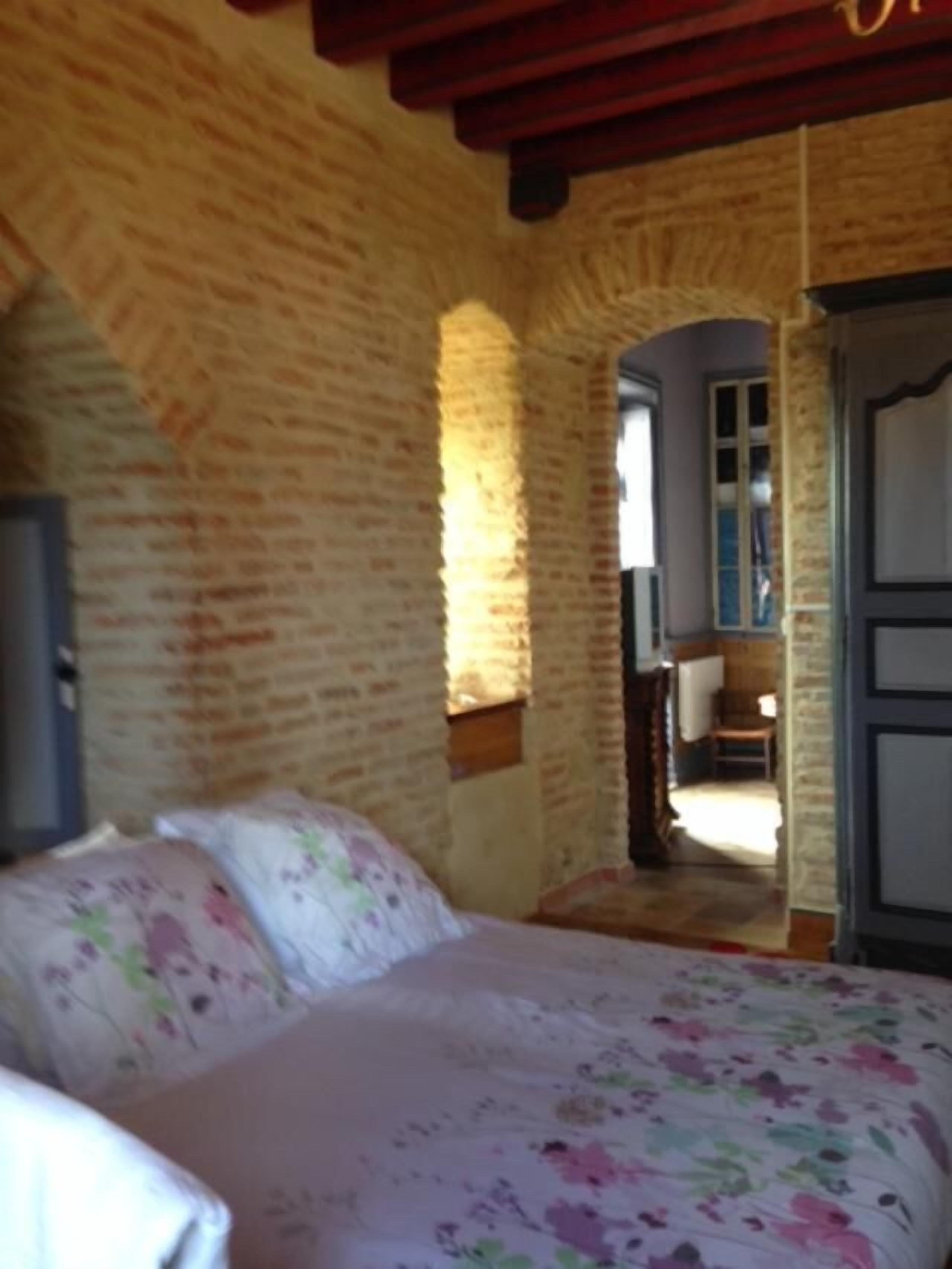 A bedroom with a brick wall, a bed with floral bedding, and a door leading to another room.