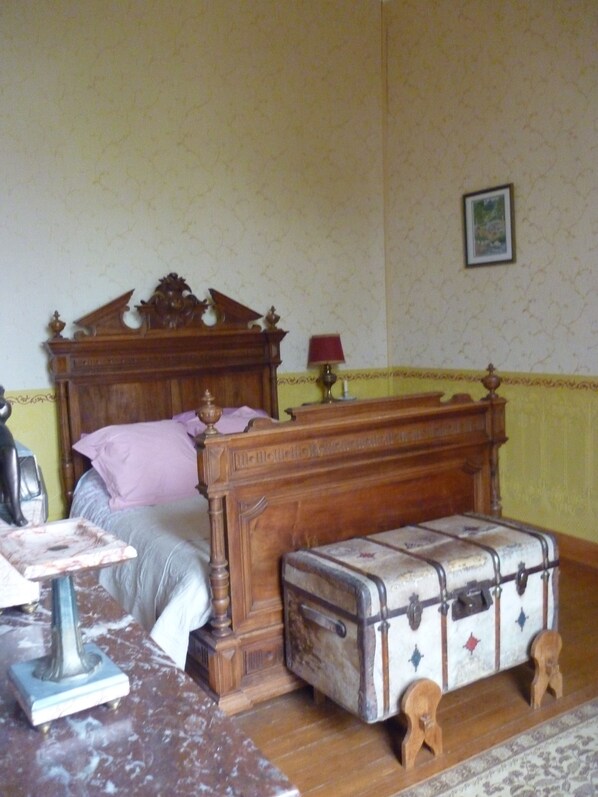 Un dormitorio con una cama de madera, una mesita de noche con una lámpara y una maleta antigua.