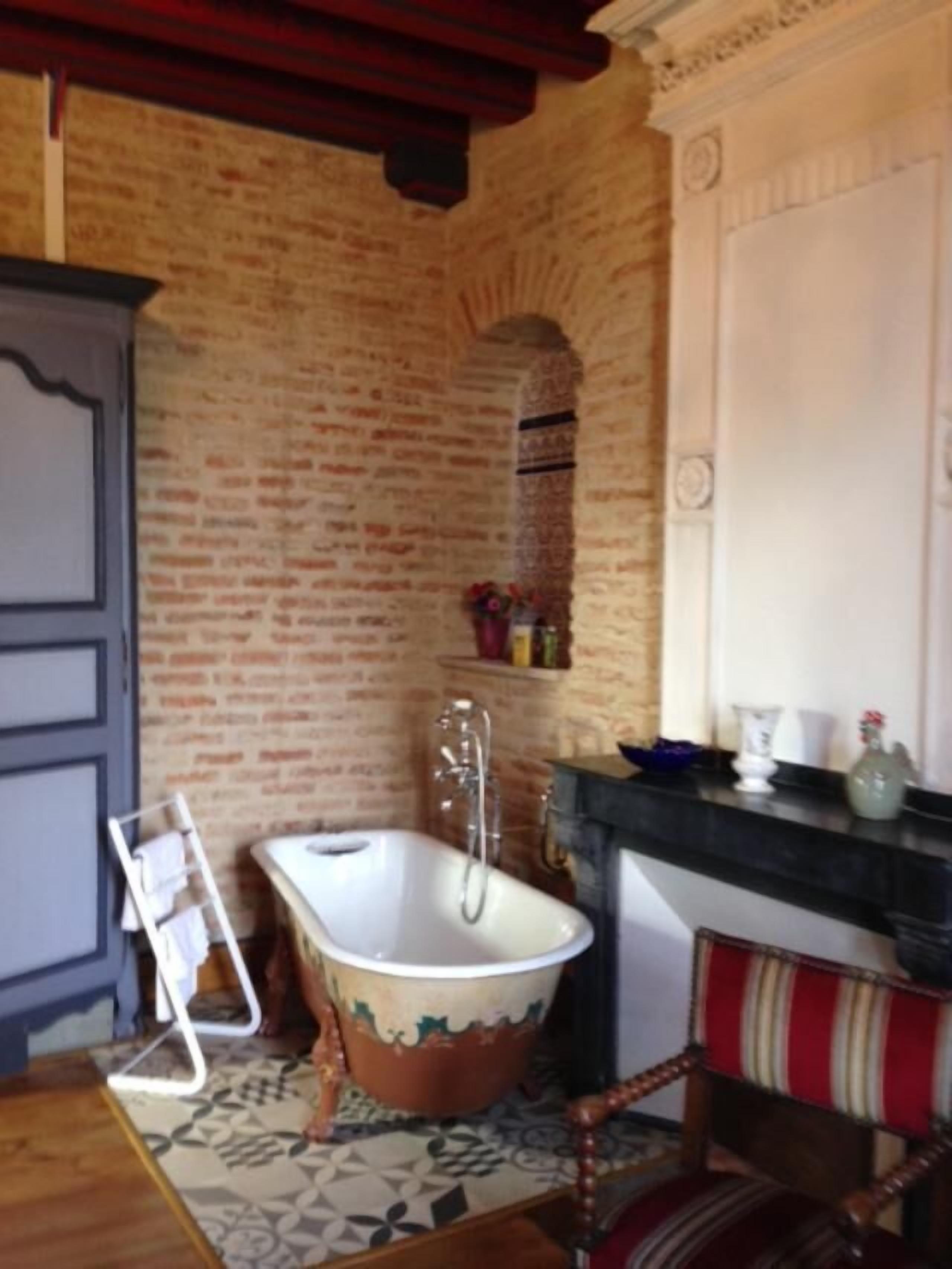 Un baño con una bañera de patas de león, una silla de madera, un perchero para toallas y una pared de ladrillo.