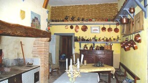 Una cocina tradicional con un horno de ladrillo, un candelabro sobre la mesa y diversos utensilios de cocina y utensilios de cocina en las paredes.