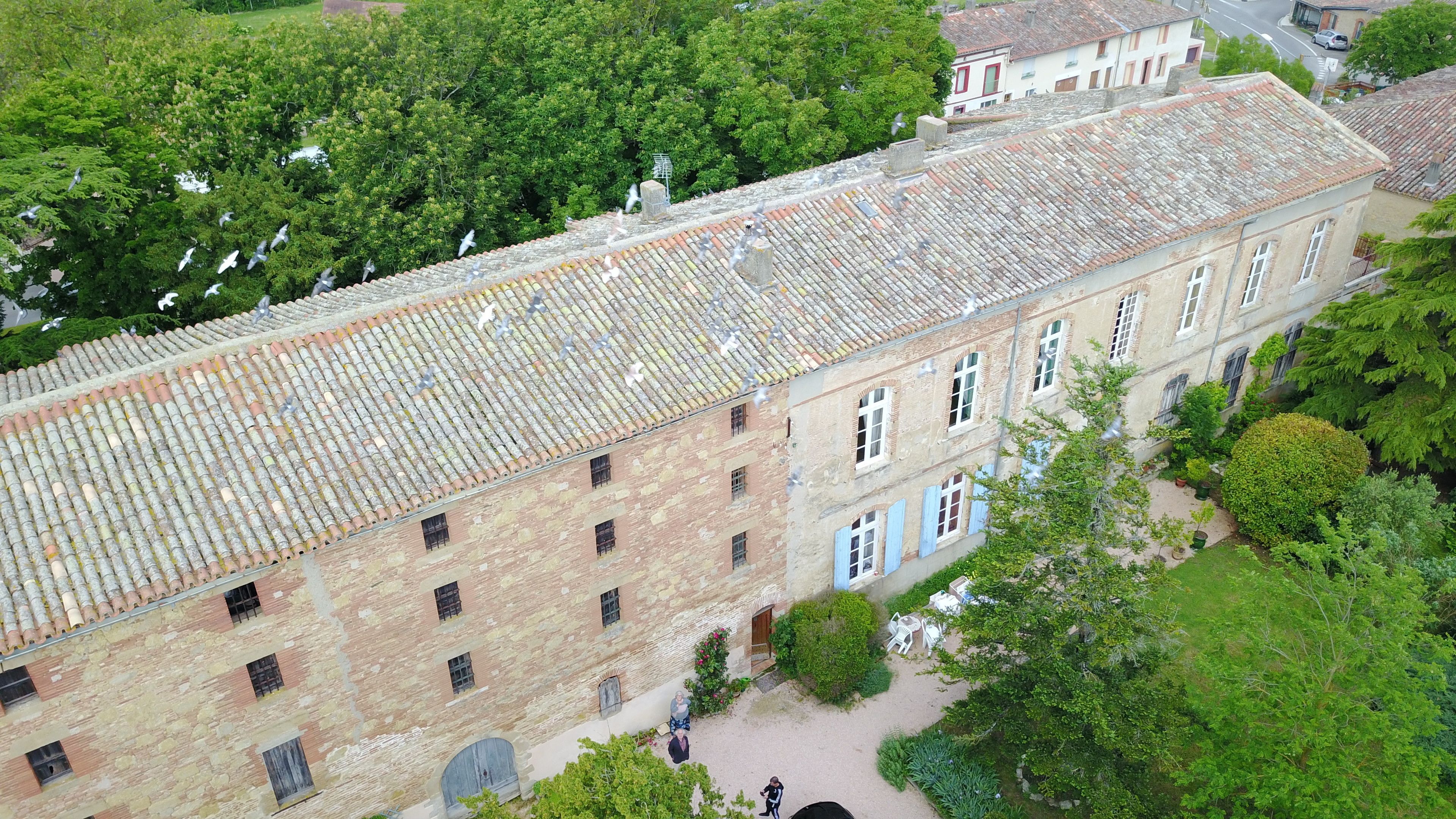 Un bâtiment historique, doté d’un toit en tuiles et de murs en briques, entouré d’une végétation luxuriante.