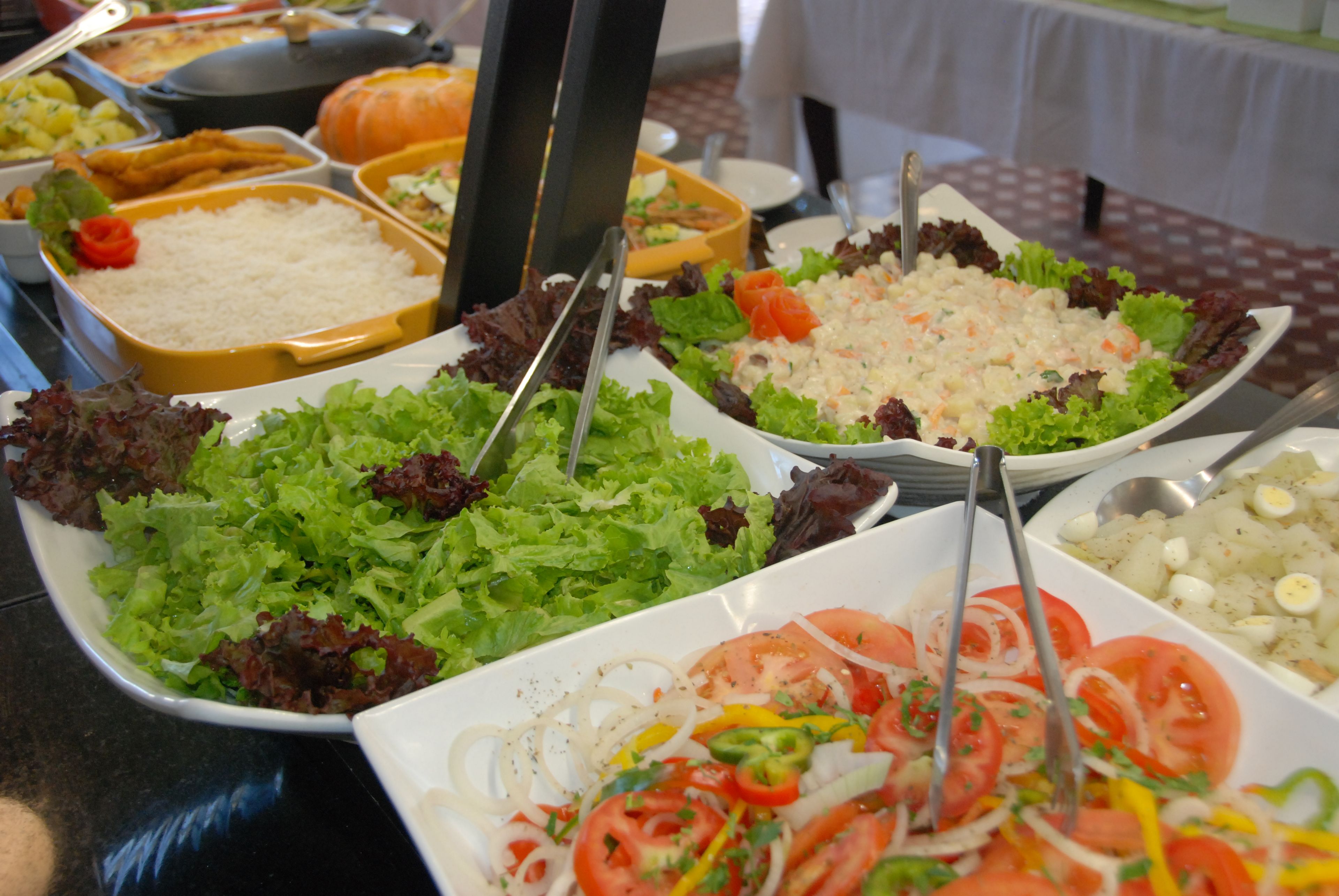 Un bufé con diversos platos, incluyendo ensaladas, arroz y otros alimentos preparados.