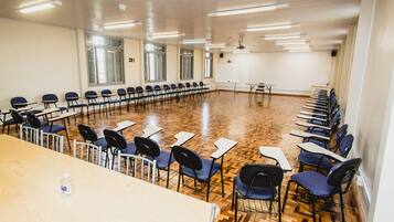 A conference room with a long table and rows of chairs, wooden flooring, and large windows.