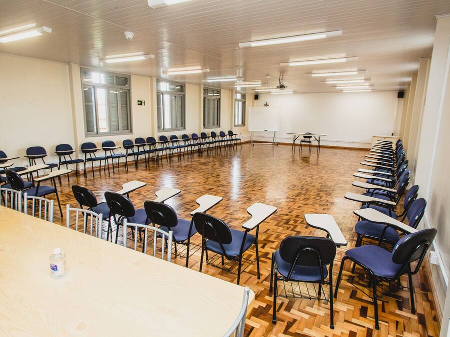 A conference room with a long table and rows of chairs, wooden flooring, and large windows.